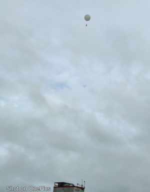 Ballon sonde dans le ciel de Matoury. Le ballon et le parachute sont visibles, la sonde est plus bas hors de l'image.
